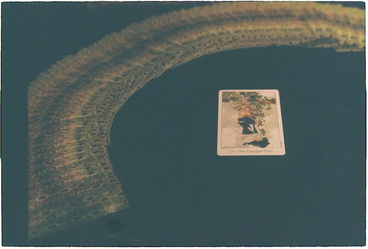 A vintage tarot card layout featuring The Hanged Man amidst a spread of cards on a dark surface.